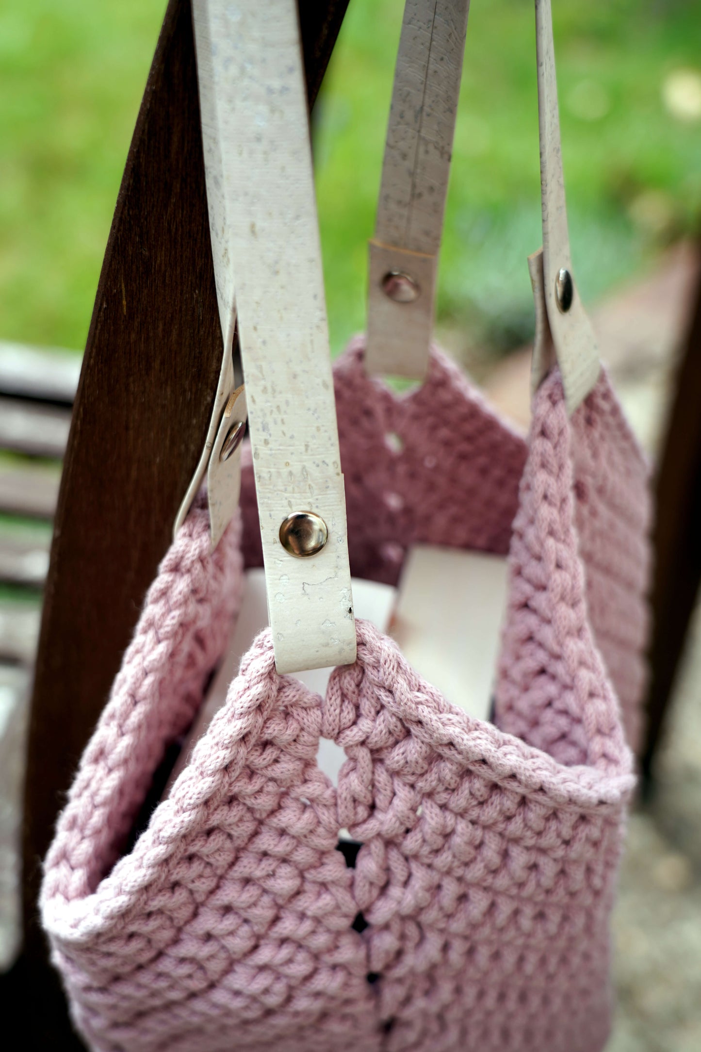 Pink knitted bag with white straps against a blurred green background