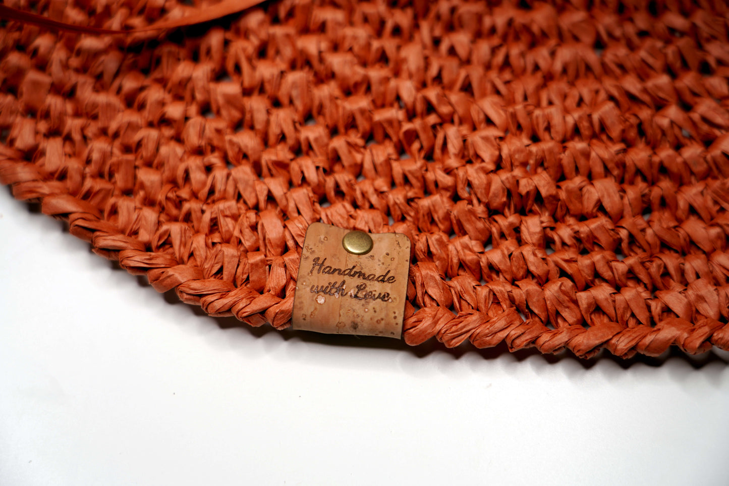 Close-up of a woven orange mat with a 'Handmade with Love' label on a white background