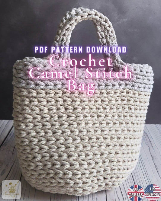 A large chunky crocheted camel-stitch tote bag in a warm cream or camel tone, shown against a dark gray background on a light wood surface. Pink text overlays read 'PDF PATTERN DOWNLOAD' and 'Crochet Camel Stitch Bag'.