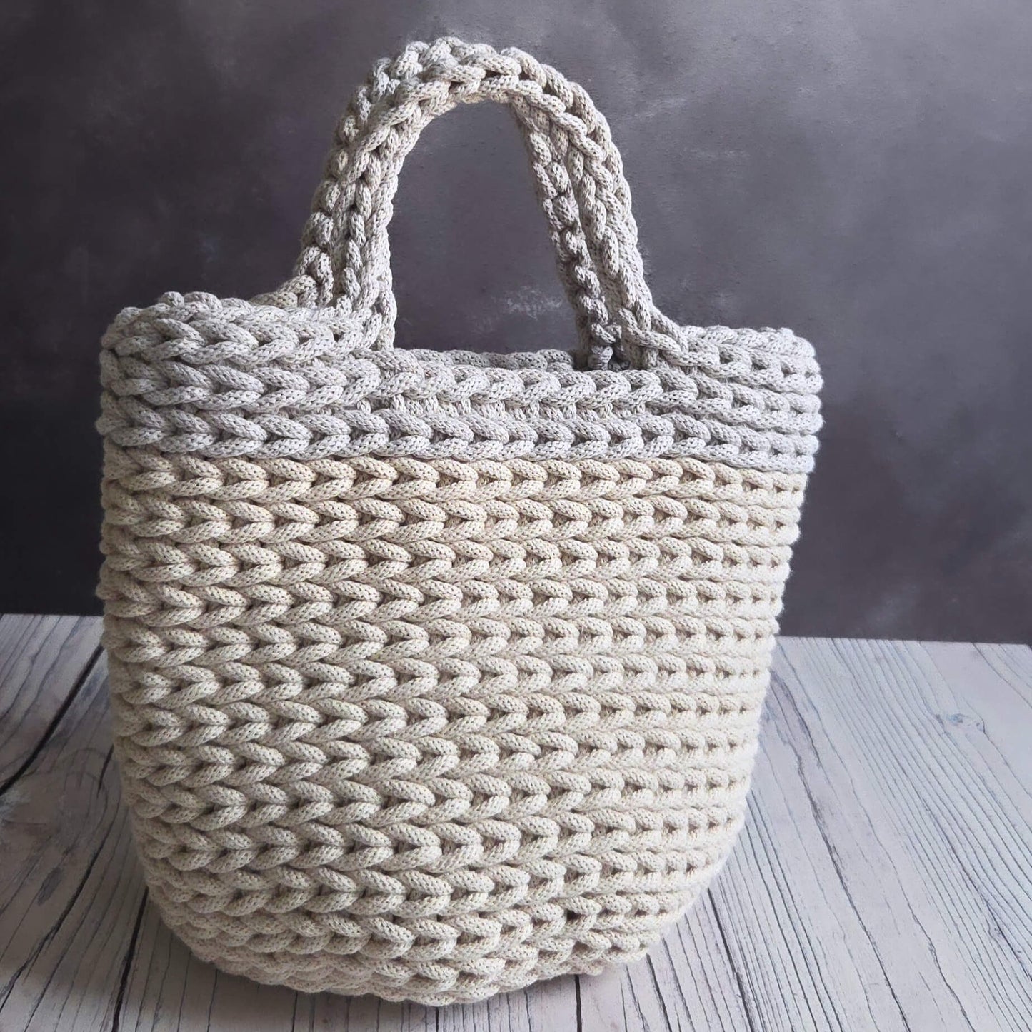 Beige woven tote bag on a wooden surface with a dark background