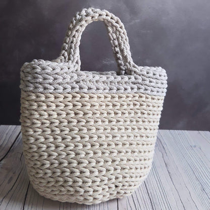 Beige woven tote bag on a wooden surface with a dark background