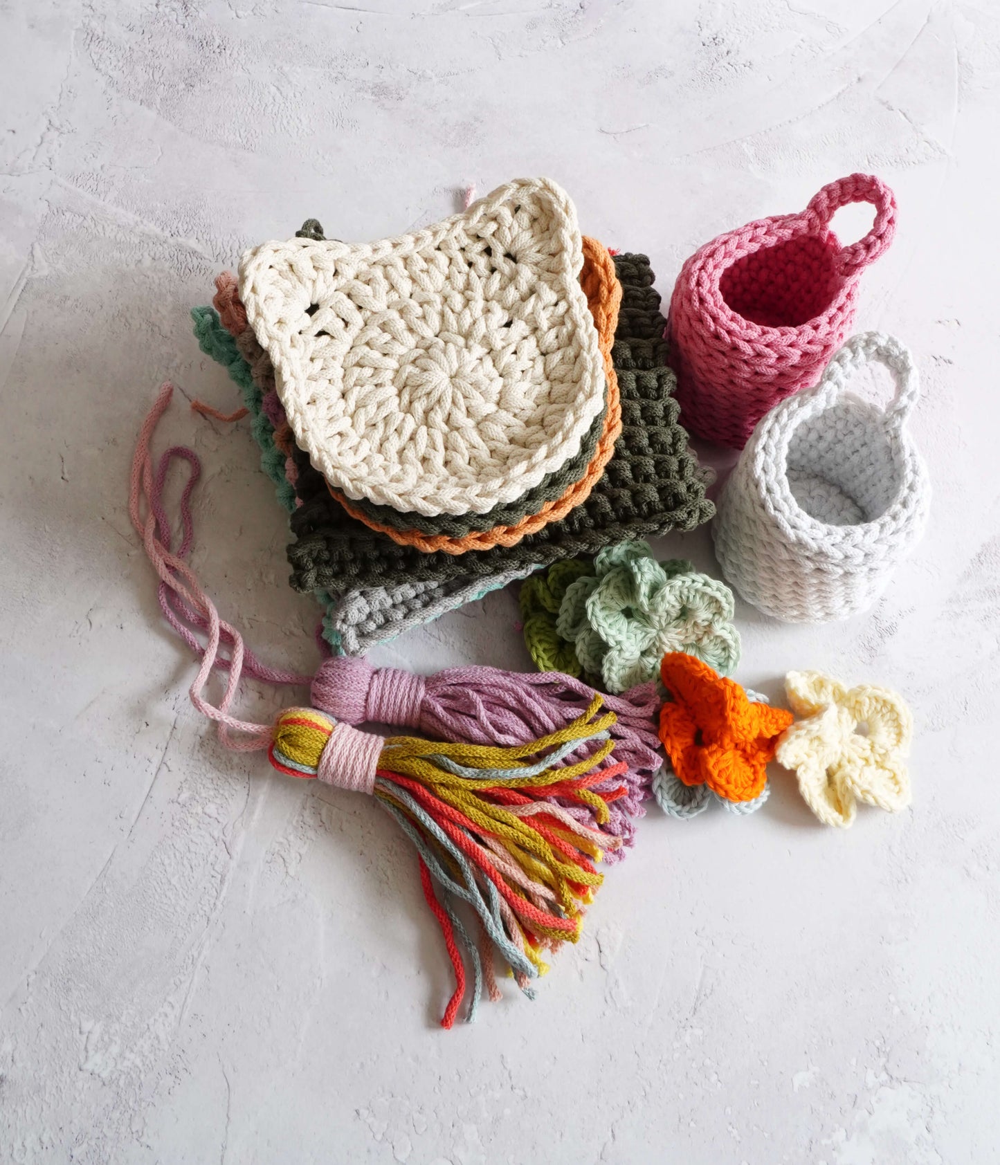 Collection of crocheted items including a pouch, tassels, and yarn on a light surface.