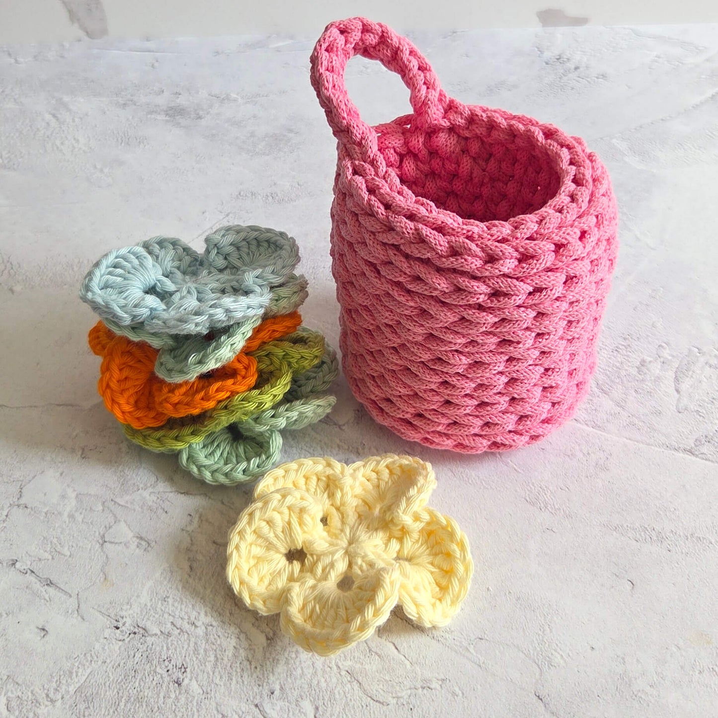 Pink crocheted basket with colorful crocheted flowers on a light surface