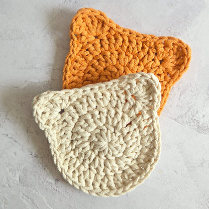 Two crocheted pot holders, one orange and one beige, on a light gray surface.