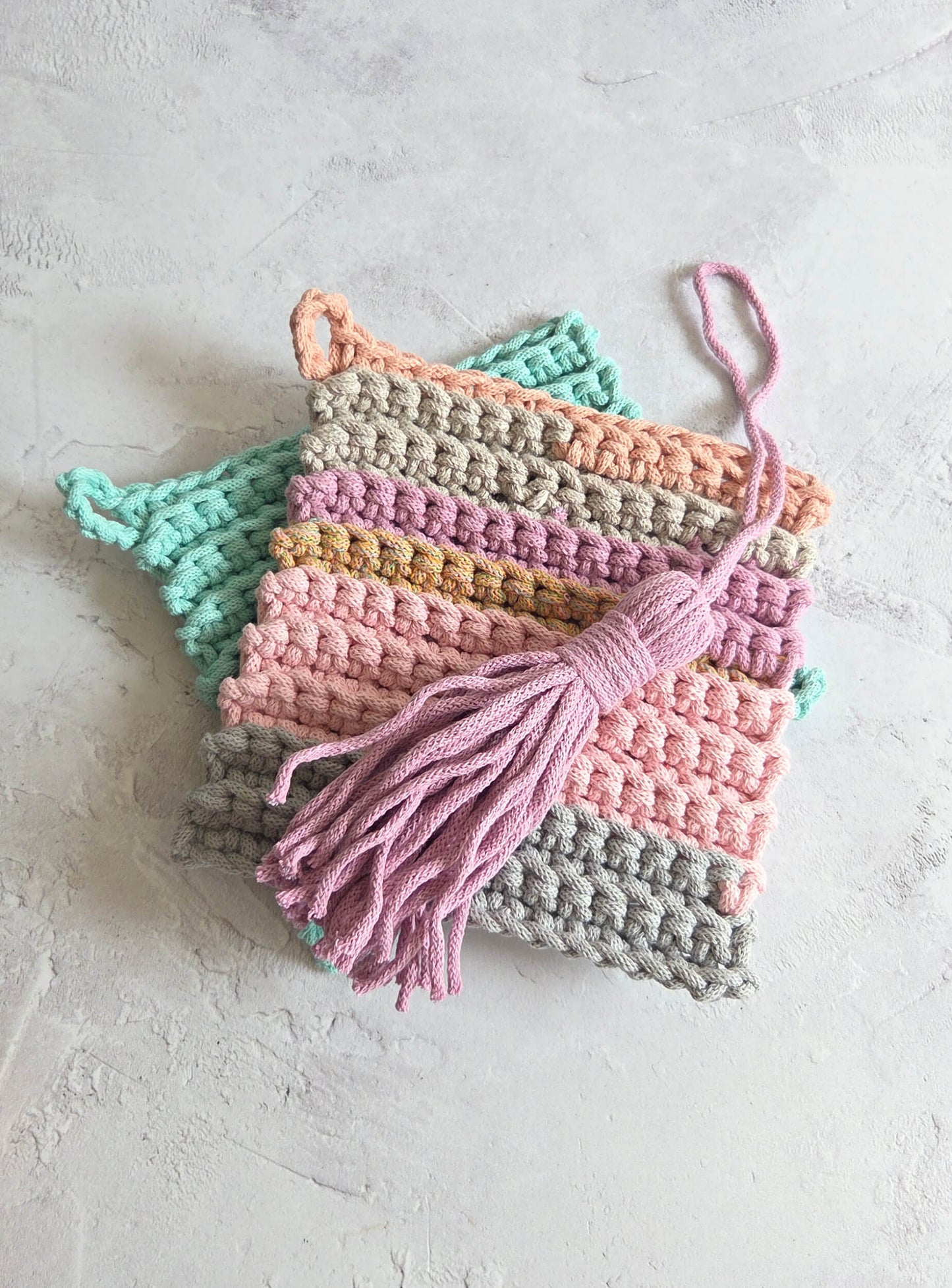 Colorful crocheted potholders with tassels on a light gray background