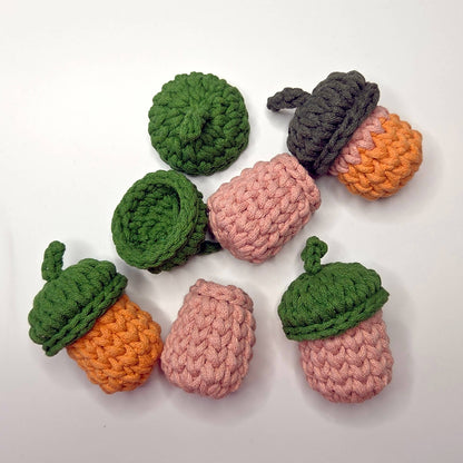 Six crocheted acorn-shaped items in green, pink, and orange yarn, arranged on a plain white background.