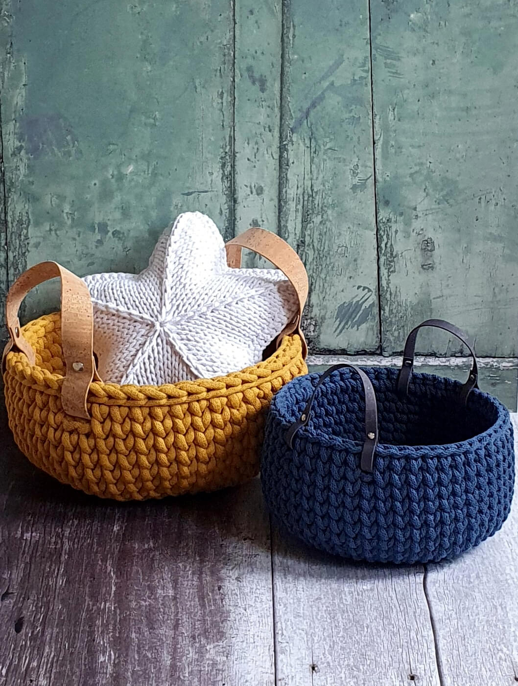 Two knitted baskets, one yellow and one blue, with a white knitted item on the yellow basket against a wooden background.