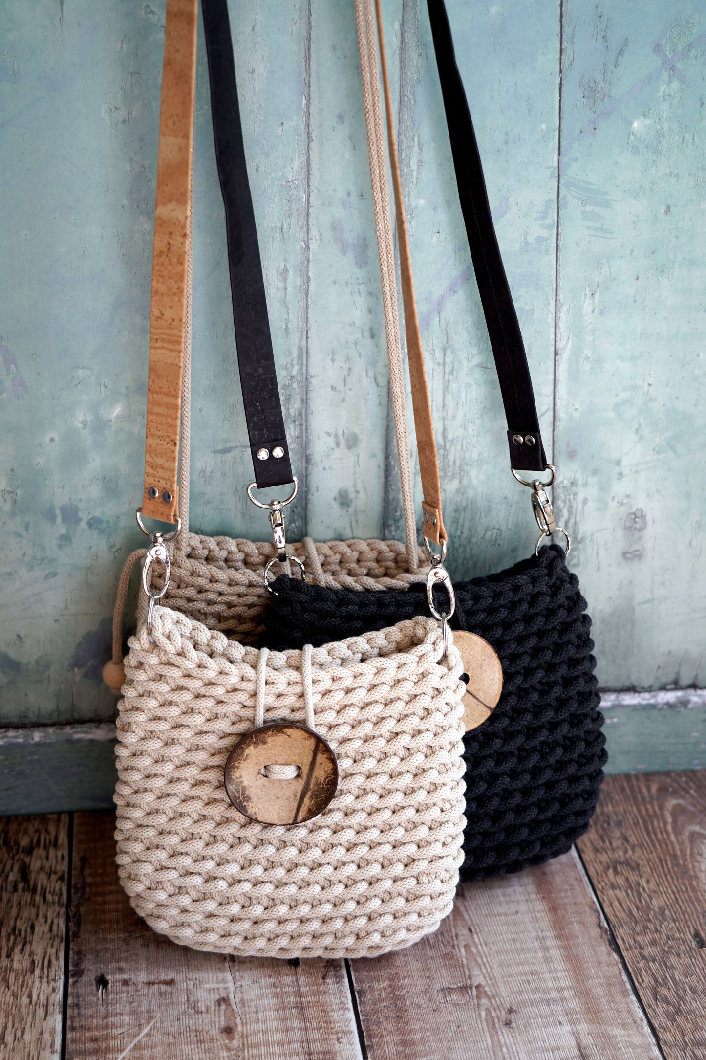 Two woven handbags, one beige and one black, with wooden accents, against a rustic wooden and blue wooden panel background.