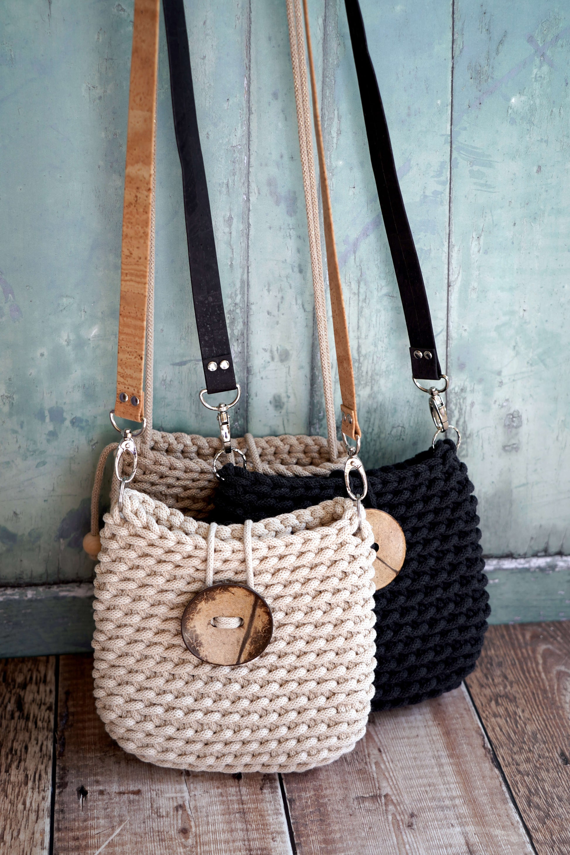 Two woven handbags, one beige and one black, with wooden accents, against a rustic wooden and blue wooden panel background.