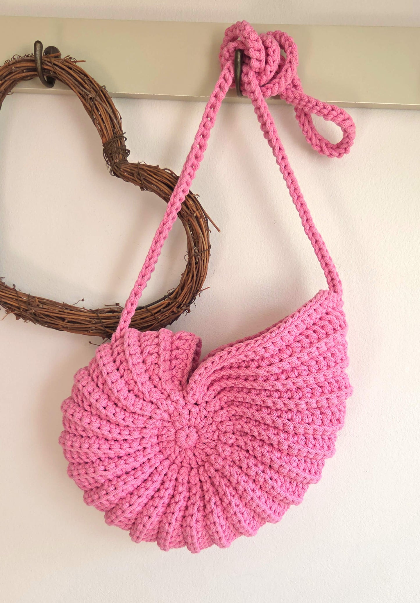 Pink crocheted bag with a strap on a white background
