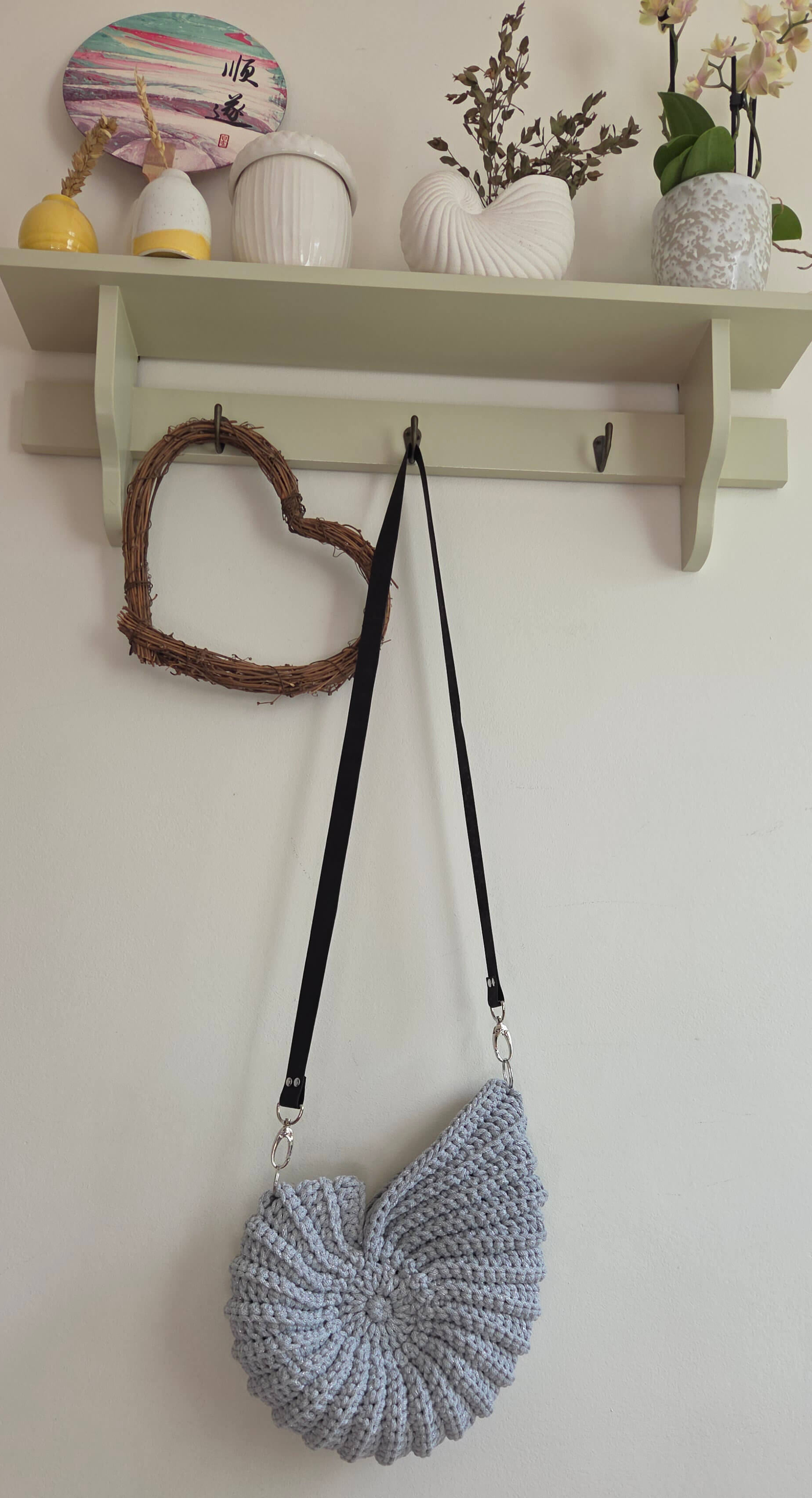 Crocheted heart-shaped bag on a hook with decorative items on a shelf in the background.