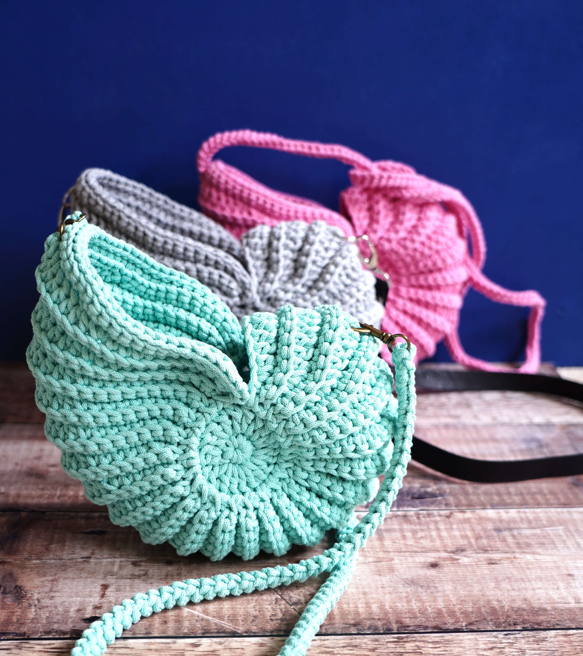 Two knitted bags, one green and one pink, on a wooden surface with a dark blue background.