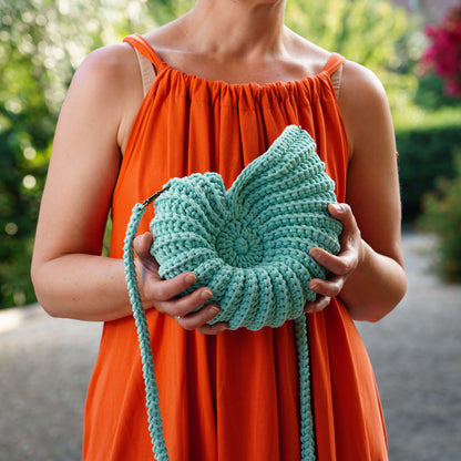 Person wearing an orange dress holding a green knitted bag outdoors.