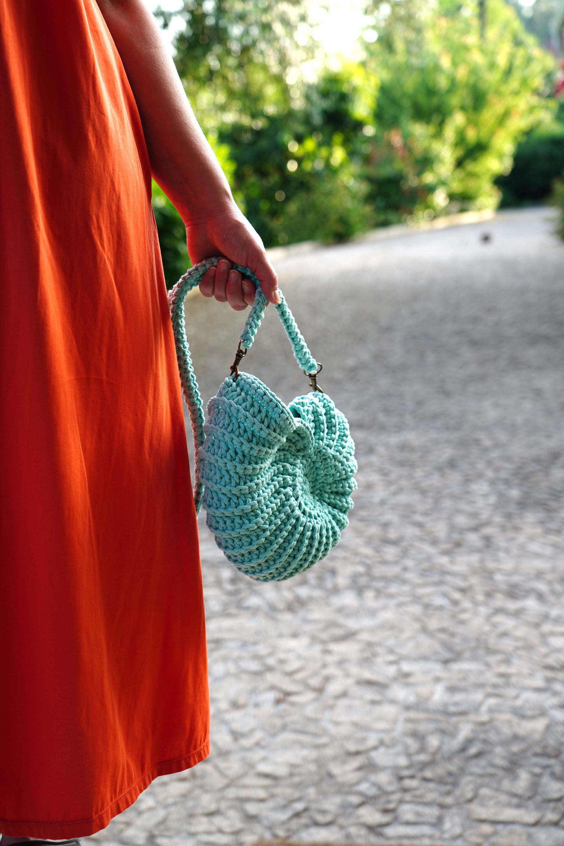 Person holding a green crocheted bag with a blurred outdoor background