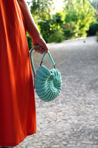Person holding a green crocheted bag with a blurred outdoor background