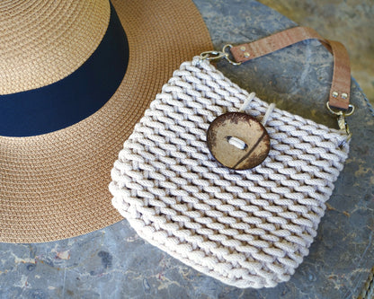 Woven handbag with coconut button and straw hat on a textured surface