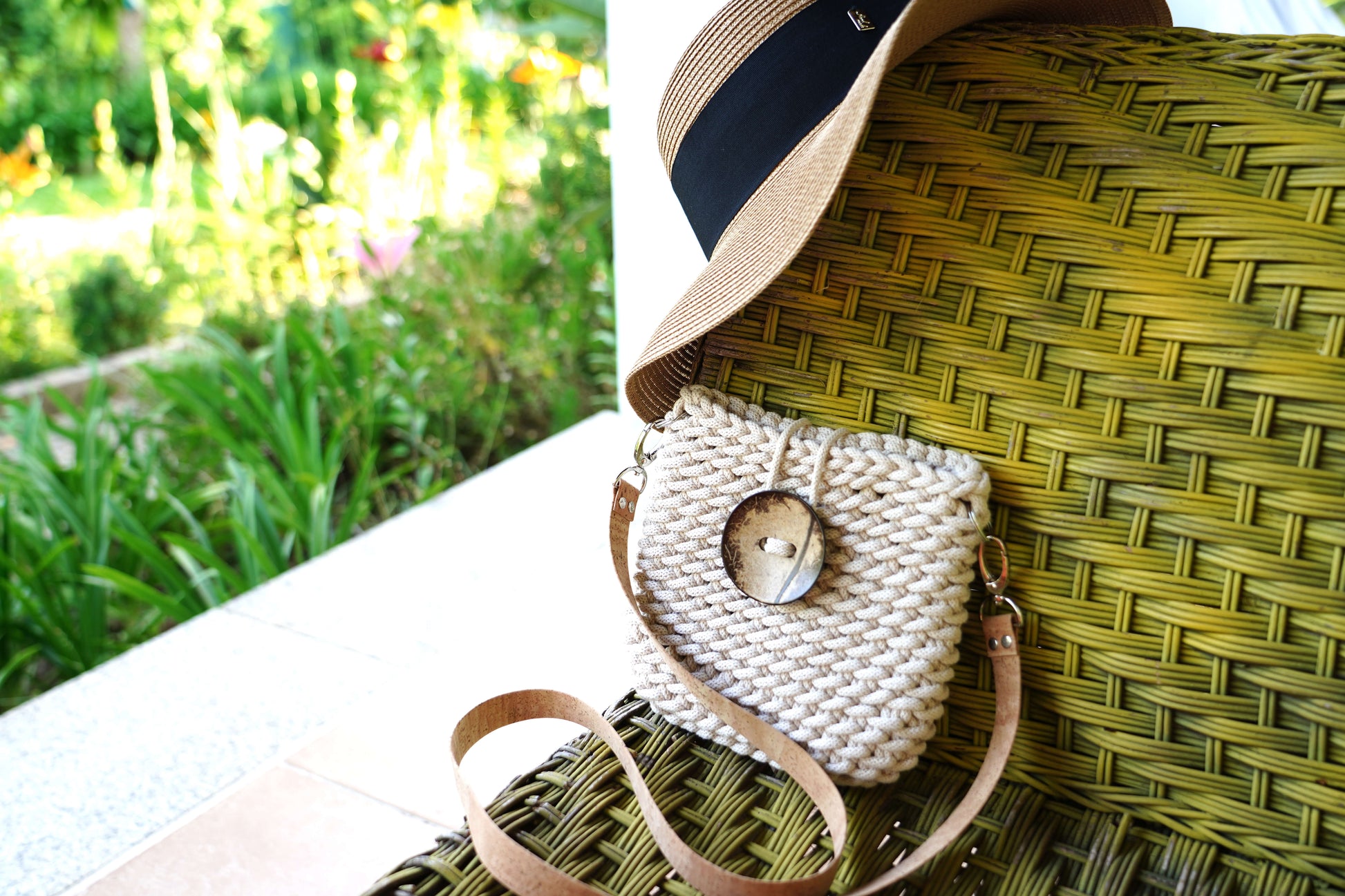 White knitted purse with a brown strap on a green woven chair outdoors.