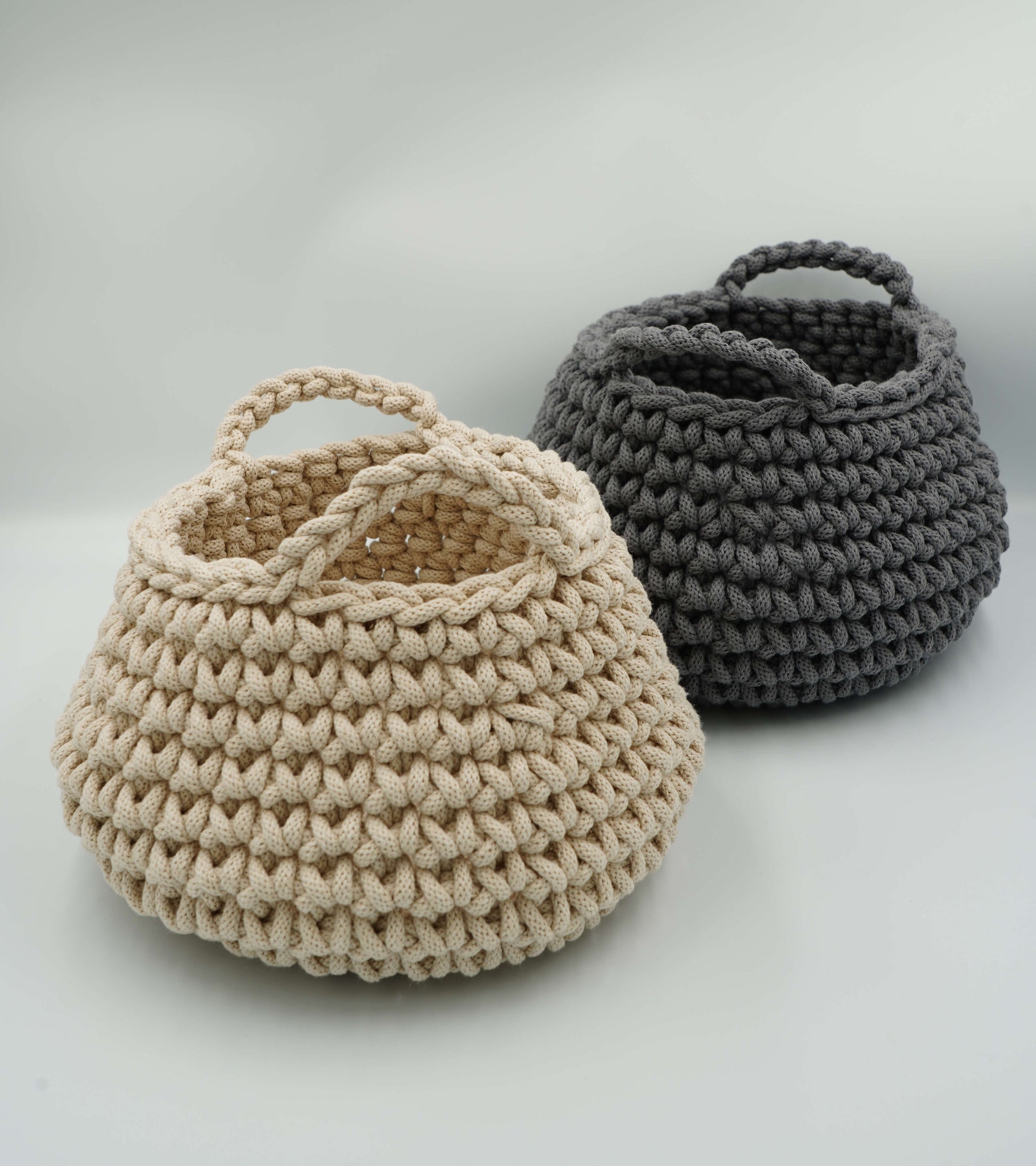 Two crocheted baskets, one beige and one gray, on a light gray background.