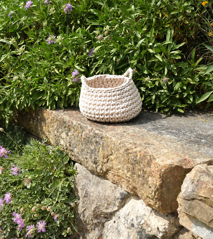 Crocheted basket on a stone ledge with greenery and flowers in the background