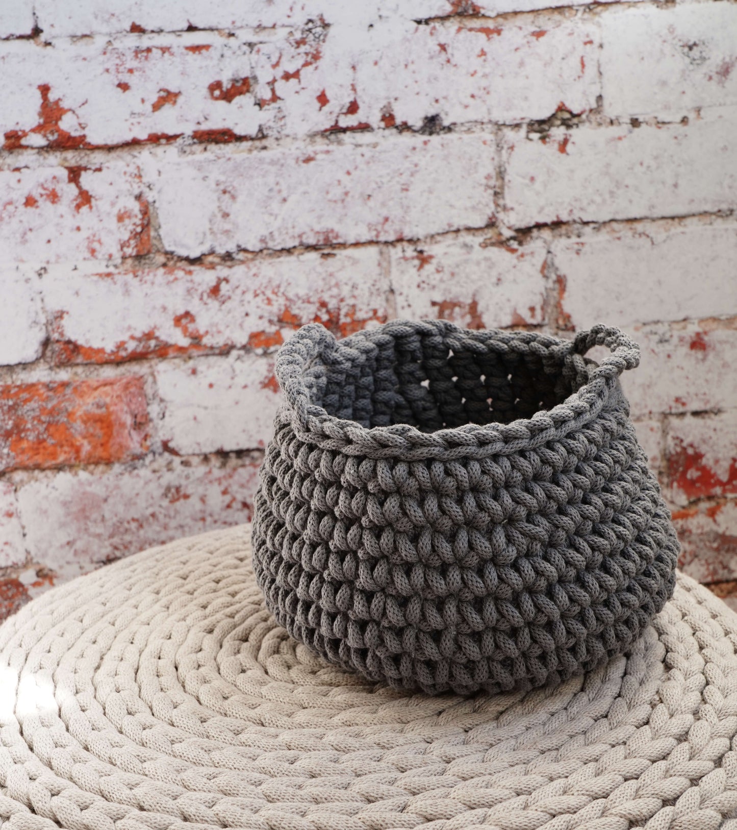 Gray knitted basket on a textured surface with a brick wall background