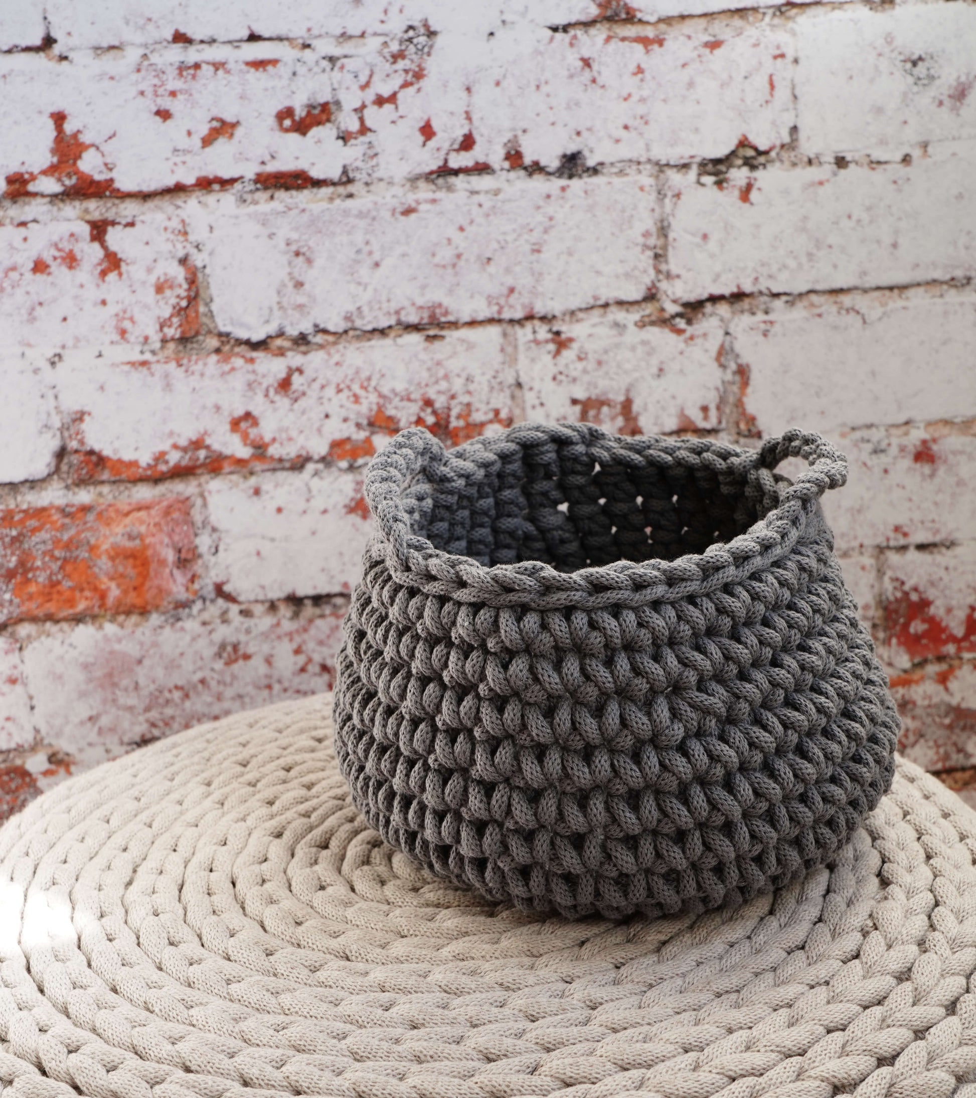 Gray knitted basket on a textured surface with a brick wall background