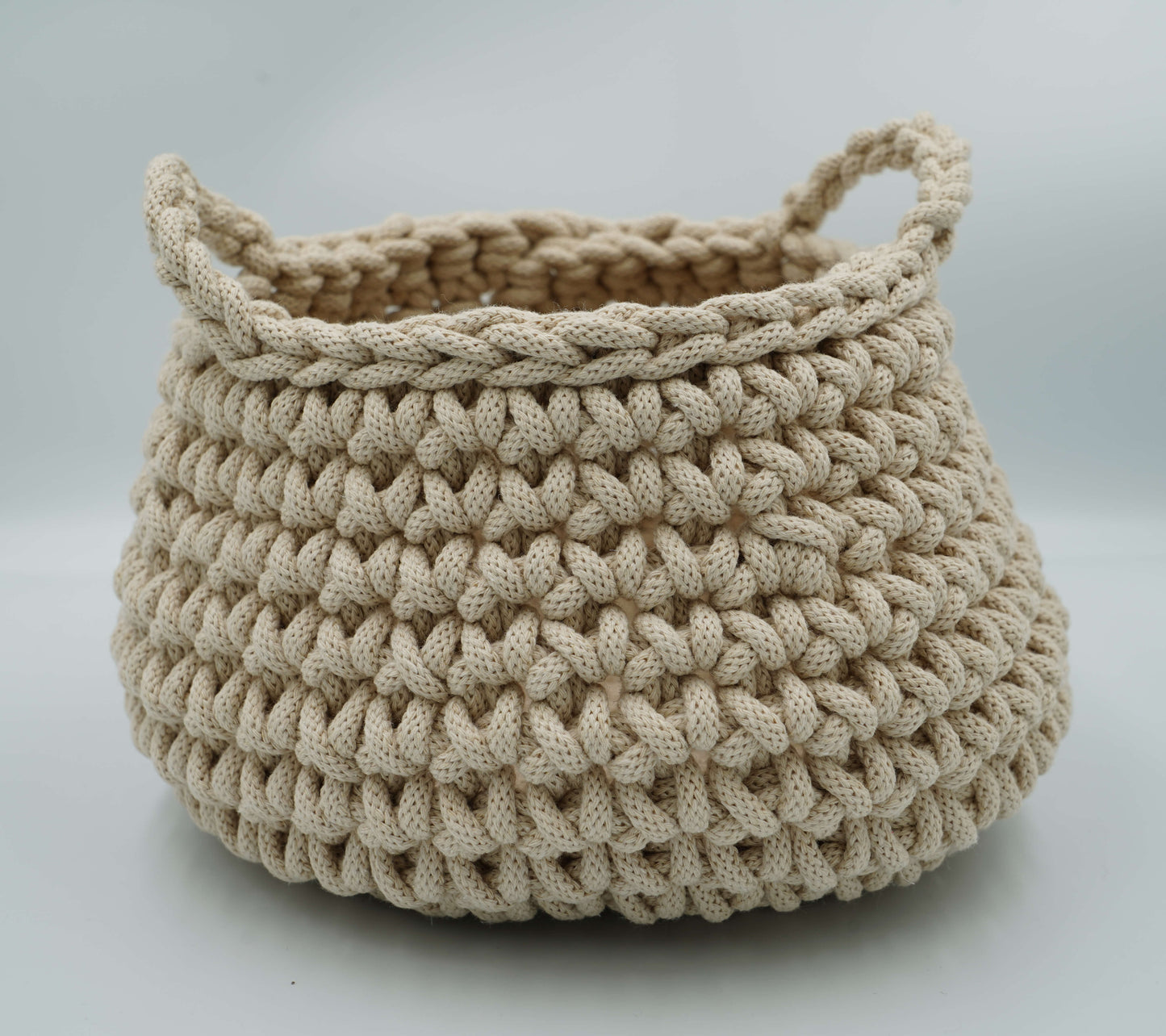Beige crocheted basket with handles on a light gray background