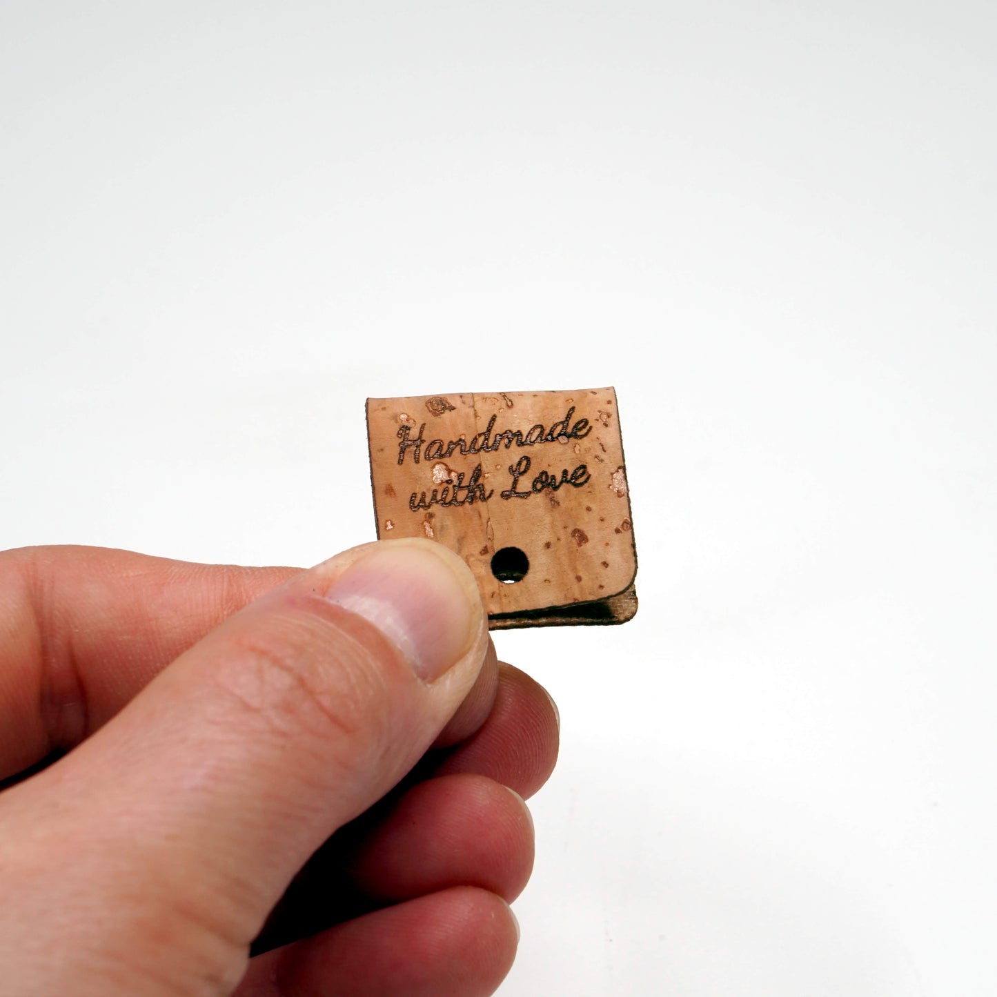 Small wooden tag with 'Handmade with Love' text held by a hand on a white background