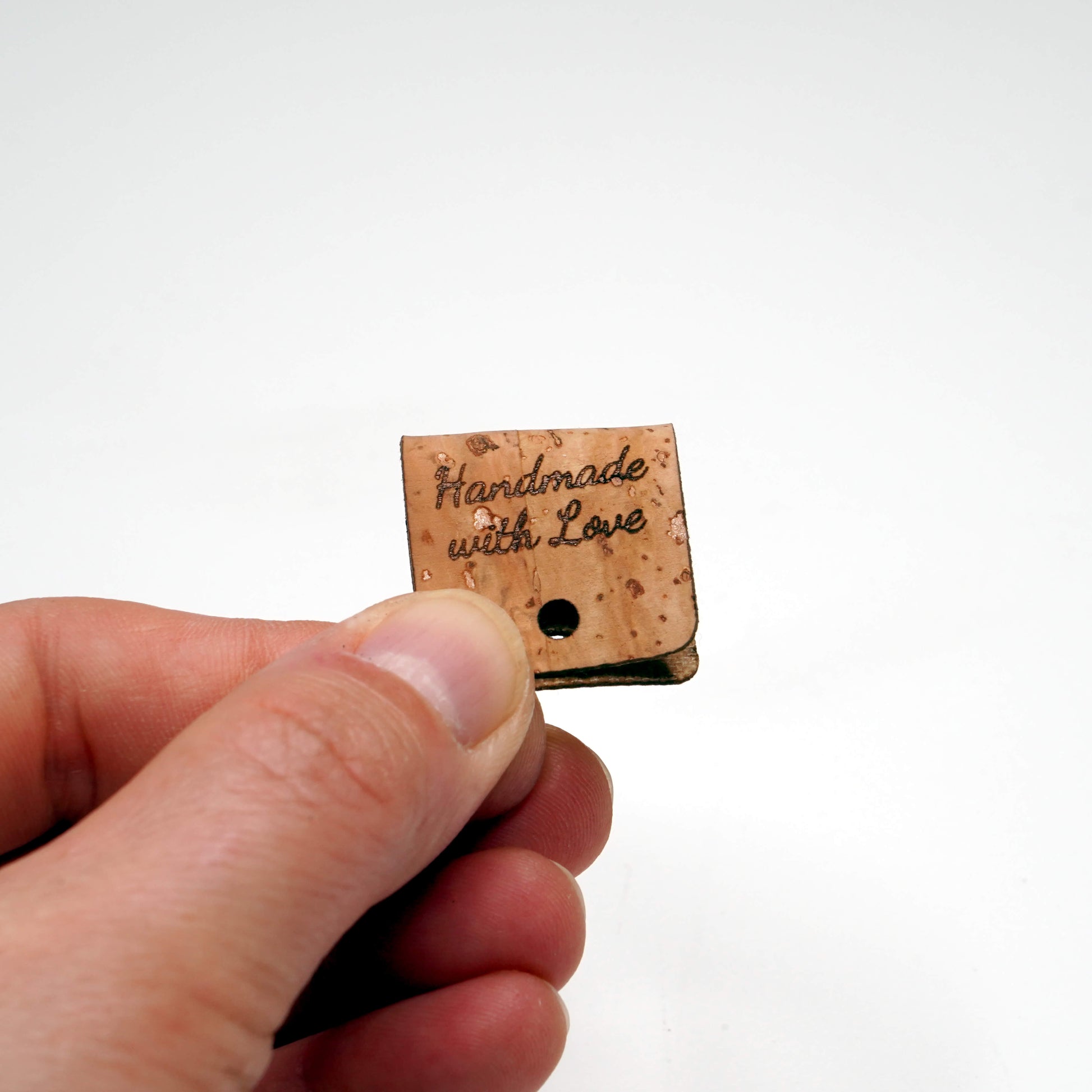 Small wooden tag with 'Handmade with Love' text held by a hand on a white background