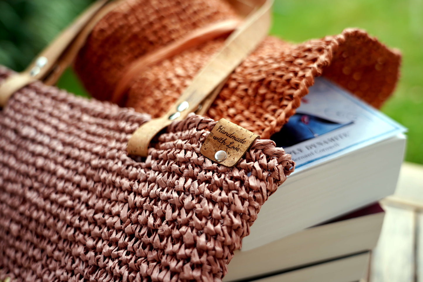 Brown woven bag with leather handle and strap, placed on a stack of books outdoors.