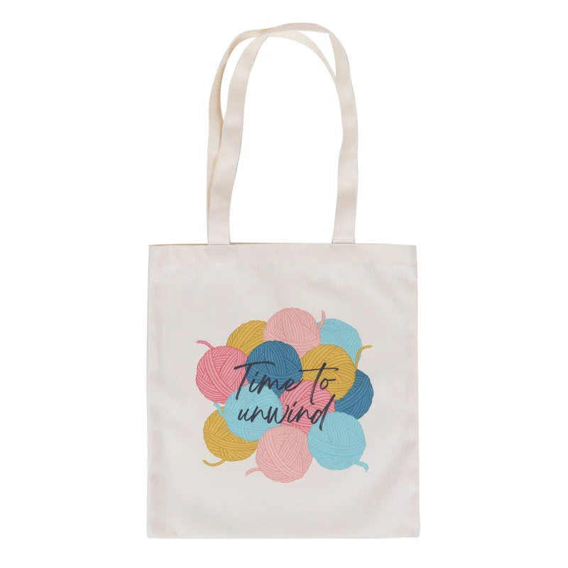Tote bag with colorful yarn balls and 'Time to unwind' text on a white background