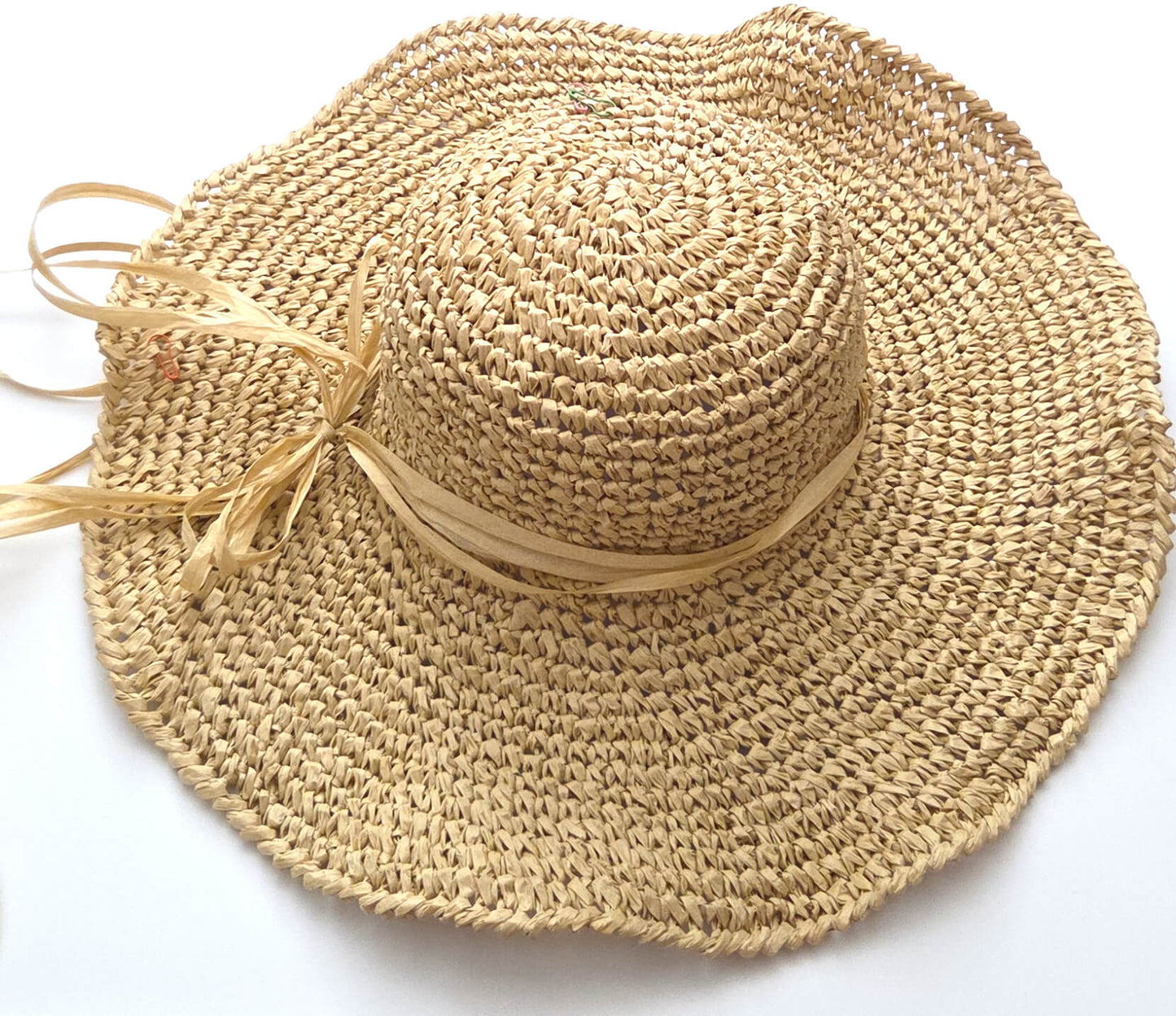 A natural straw sun hat with a wide brim, a round crown, and a matching straw ribbon tied in a bow on the side, shown on a plain white background.