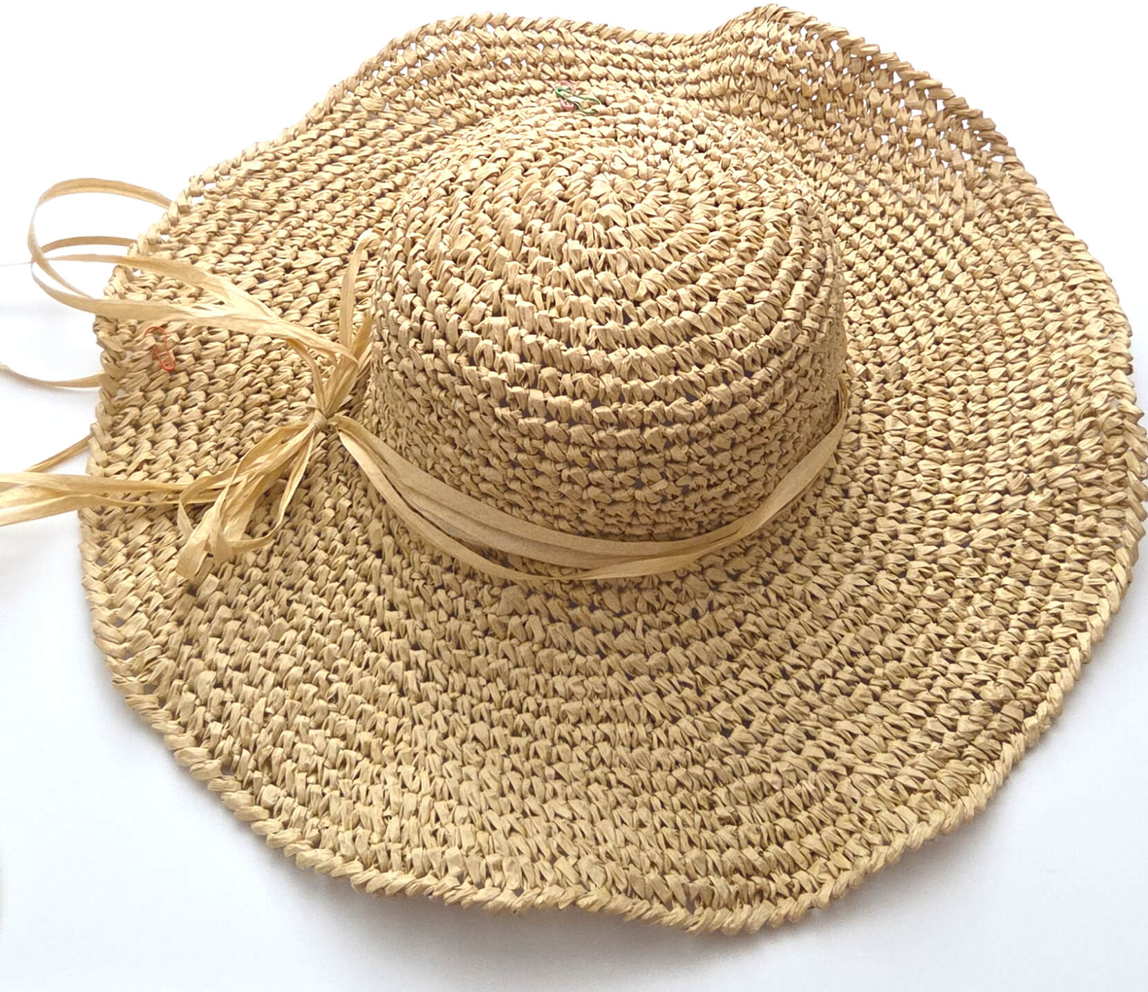 A natural straw sun hat with a wide brim, a round crown, and a matching straw ribbon tied in a bow on the side, shown on a plain white background.