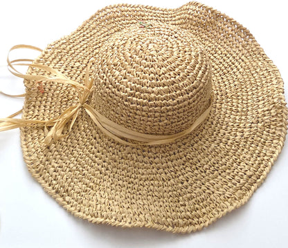 A natural straw sun hat with a wide brim, a round crown, and a matching straw ribbon tied in a bow on the side, shown on a plain white background.
