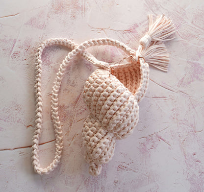 Handmade crochet shell bag with tassel on a textured pink surface