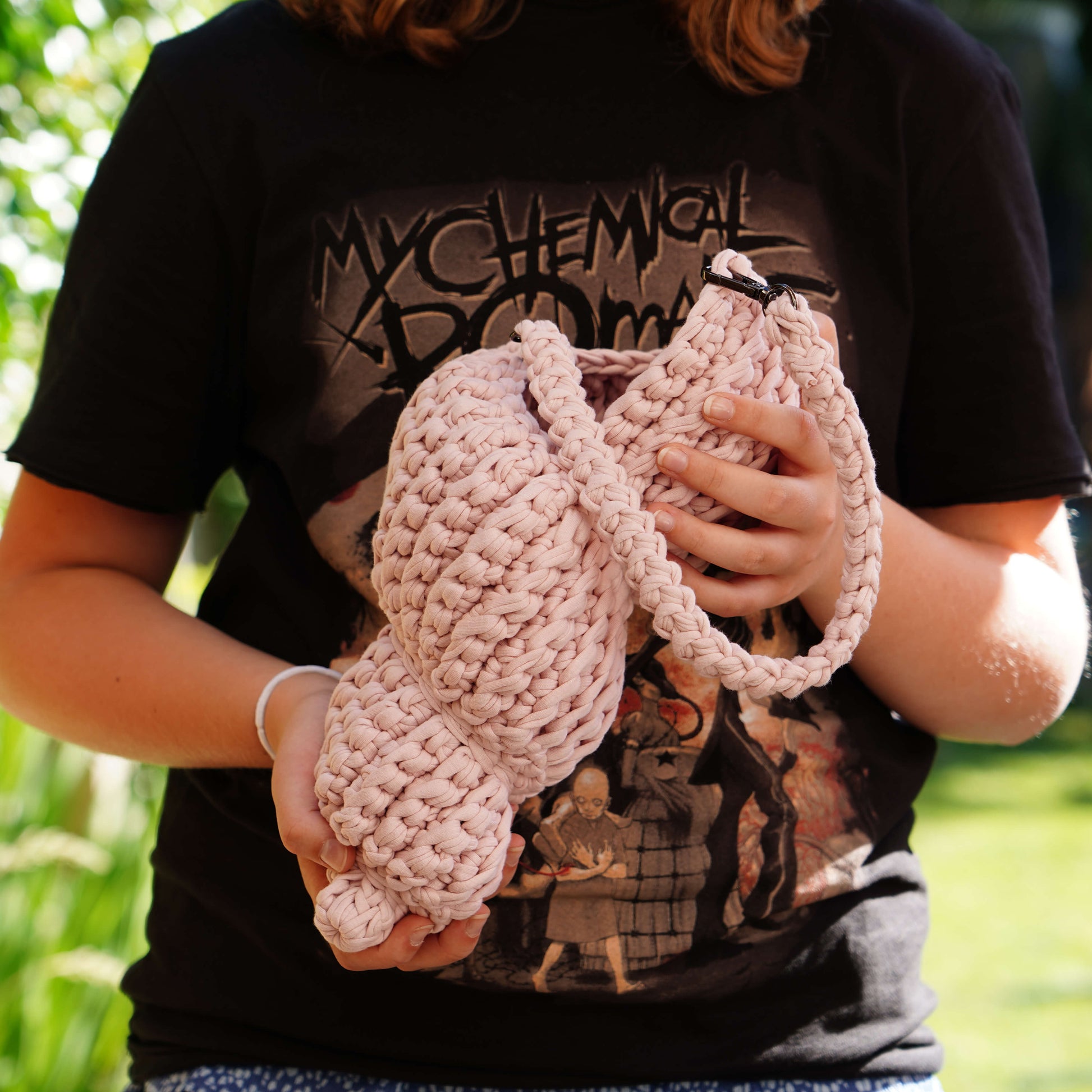 Person holding pink knitted bunny ears with a black t-shirt featuring graphics in the background.