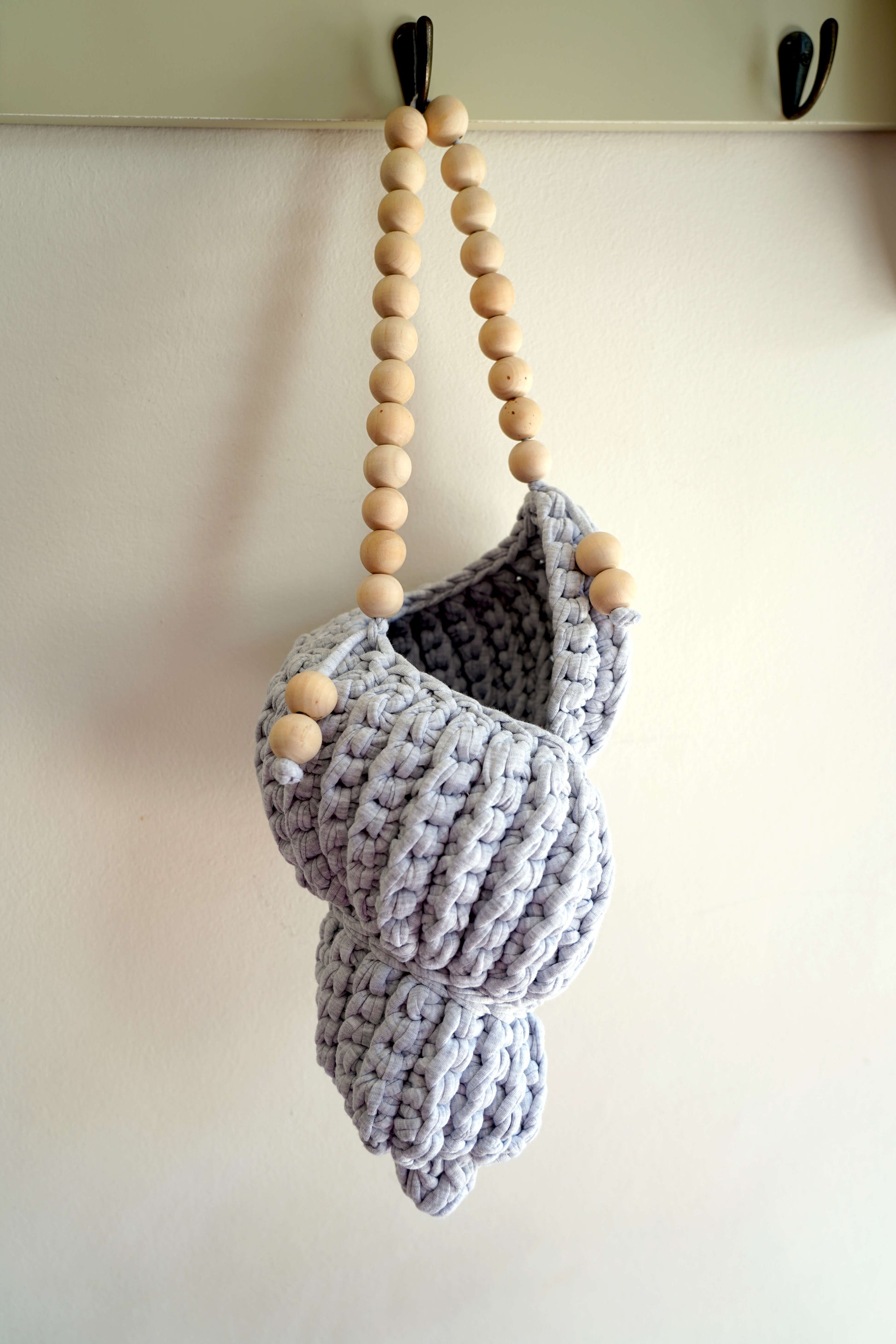 Crocheted pouch with wooden beads hanging on a hook against a white wall.